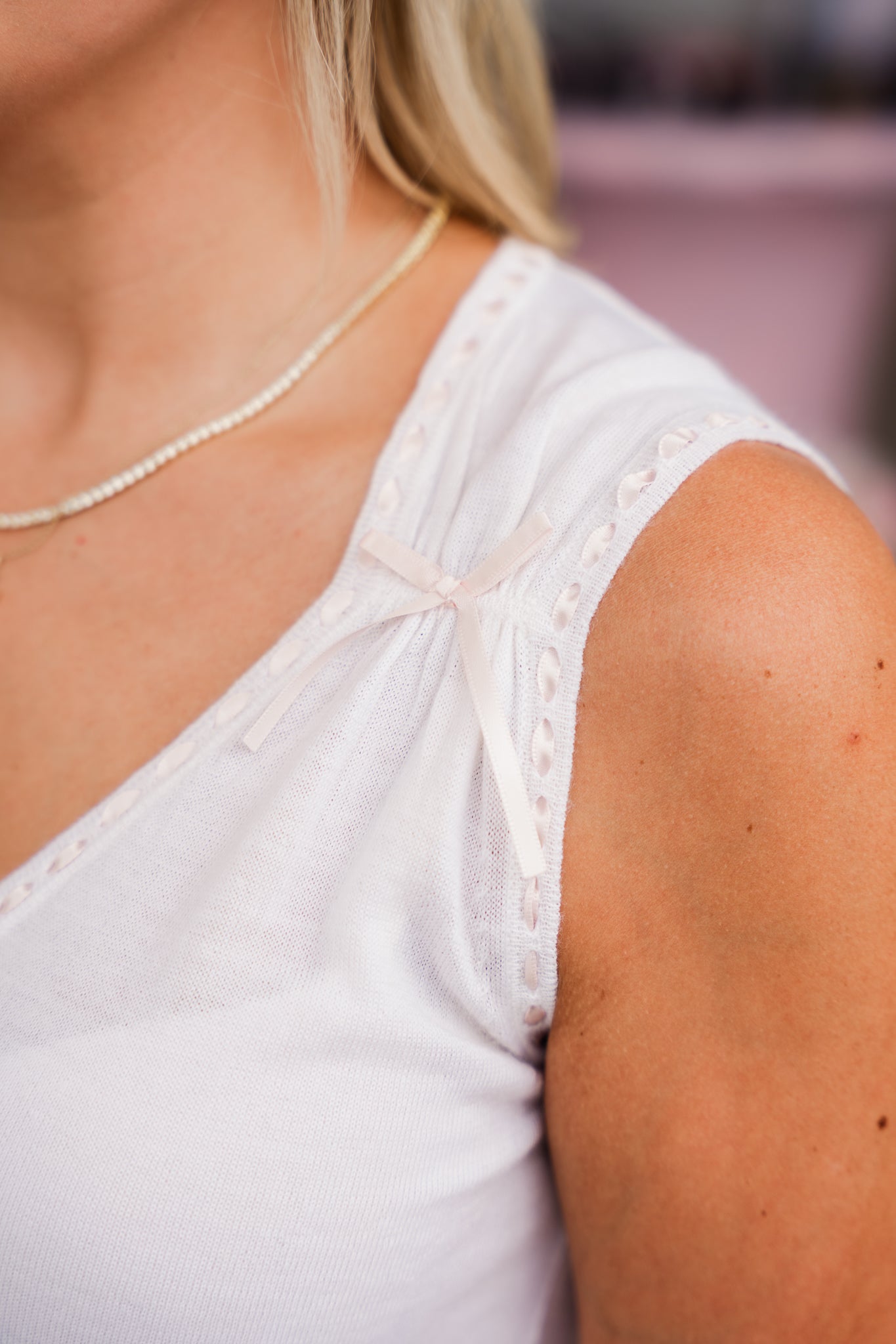 Close-up of a person wearing a white sleeveless top with lace details.