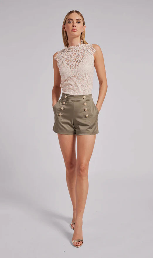 Woman wearing a lace top and olive green shorts with buttons on a gray background