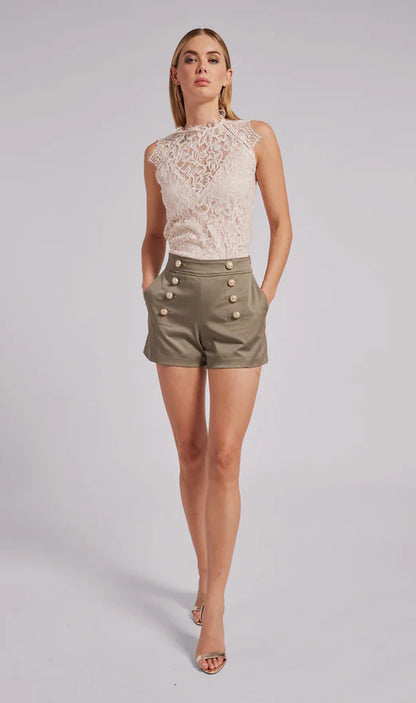 Woman wearing a lace top and olive green shorts with buttons on a gray background